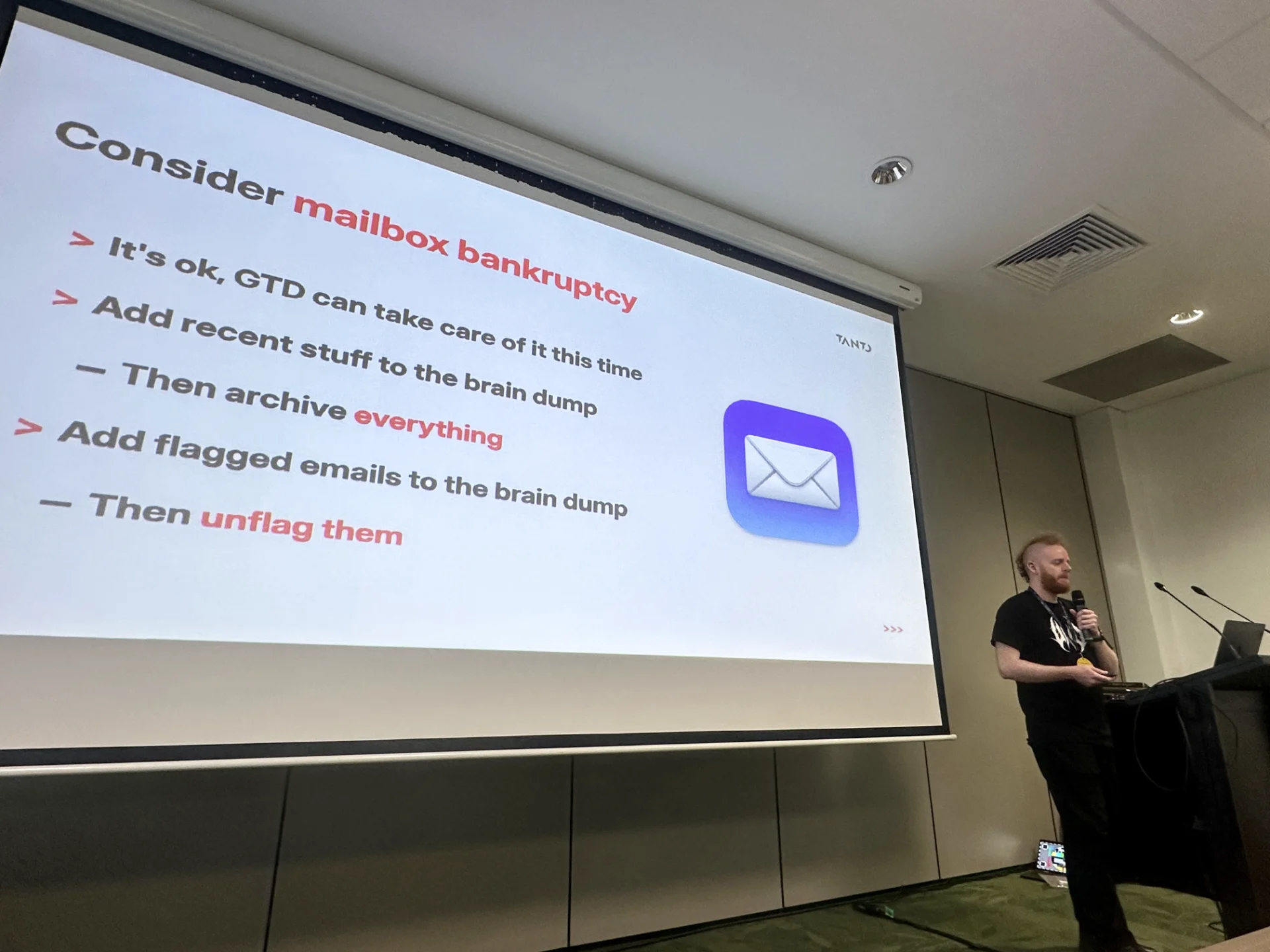 Justin standing at a lectern in front of a slide about handling a cluttered email inbox