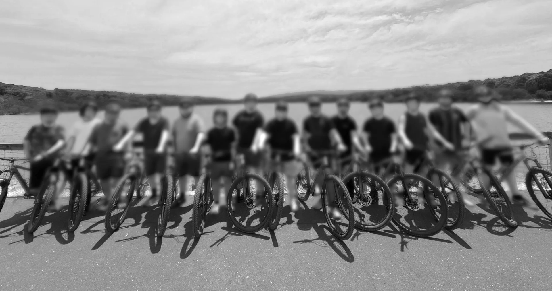 Fourteen people standing in front of a lake with mountain bikes